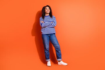 Fototapeta premium Full length photo of shiny attractive lady dressed striped shirt arms folded looking empty space isolated orange color background