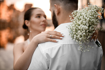 The bride's delicate hand with a wedding ring on her finger rests on the groom's shoulder