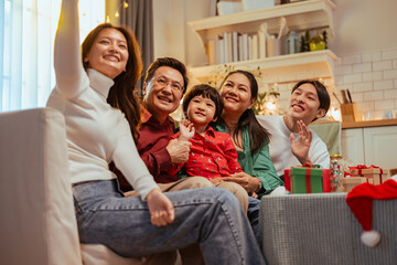 relationship, parenthood, happiness, family, enjoying, happy, care, celebration, christmas, laughing. A family of five is sitting on a couch in a living room, smiling and waving at the camera.