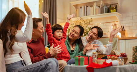 parenthood, family, party, relaxation, happy, celebrate, greeting, xmas, present, christmas. A family of four is sitting on a couch in a living room, with a young boy holding his hands up in the air.