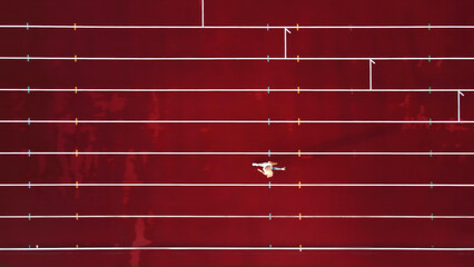 Aerial view of athlete on red track field. A lone athlete runs on a striking red track, captured...