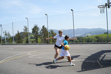 Mother teaching son how to play basketball outdoors