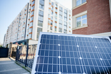 Obraz premium Photovoltaic solar panel in front of modern apartment building with balconies, suggesting residential or mixed-use. Concept of integration of sustainable renewable energy sources into architecture.