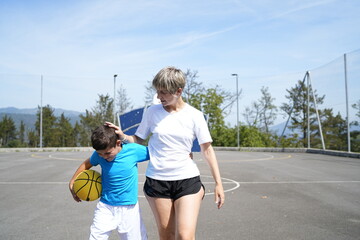 Mother and son walking on basketball court holding ball