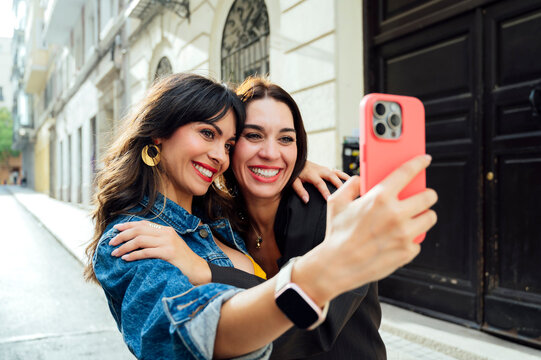Two pretty friends taking a selfie on the street