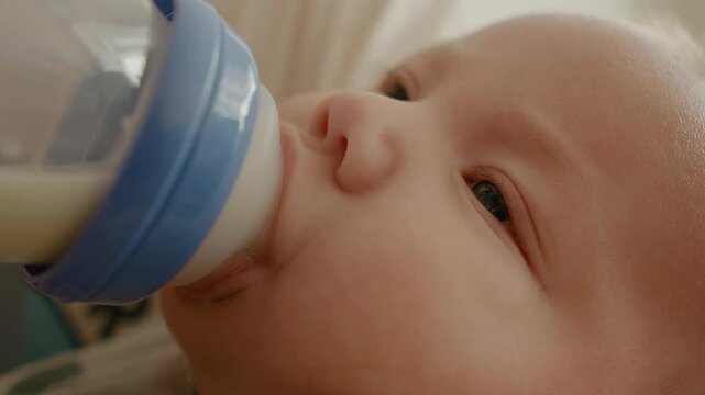 Mom feeds formula her newborn son from a bottle. Baby drinking milk from a bottle. Childcare concept.