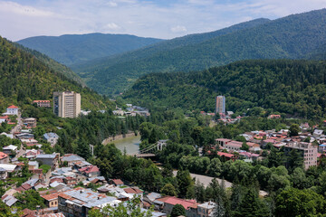 Fototapeta premium Summer view of Borjomi, Georgia, captured from Cross Mountain. The town lies nestled among green trees, with a river winding through it and surrounded by scenic mountains