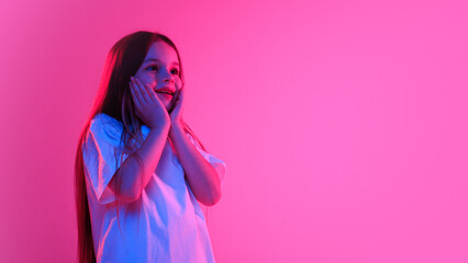 Girl, feel dreamy, holding her face and smiling with wonder in neon light against vivid gradient background. Concept of childhood, lifestyle, expressions, fashion and style, trendy. Ad