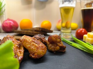 Fried chicken pieces lie on a sliced board next to glasses of beer