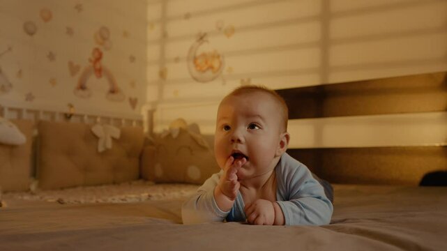 Baby boy following somebody with his eyes while massaging gums with fingers. Toddler salivating while teething in early staging of life.