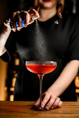 Female bartender spraying a brown cocktail in a tall stemmed glass