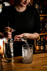 Female bartender pours a clear drink from a jigger into a change glass filled with ice cubes