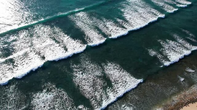Aerial video of waves breaking slowly near the shore. View from the sky. Little reef break, beach day and holidays. Located in Western Australia. Beautiful blue and clear ocean. 