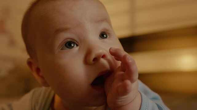 Portrait of teething baby puts his hands in his mouth while trying to keep his head up. The concept of caring for a newborn when teeth come out.
