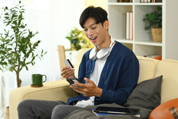 Excited asian man making an online purchase with smartphone and credit card