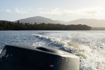 tinny dinghy boat on the water making a wake behind a boat making waves on a river in a national park in australia. beach in summer, dingy going fast