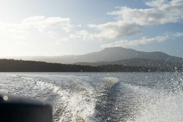 tinny dinghy boat on the water making a wake behind a boat making waves on a river in a national park in australia. beach in summer, dingy going fast