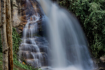 Fototapeta premium Natural background of waterfall flowing from high place through rocks and rainforest, the water flows in various ways according to the strength and beauty of the natural system.