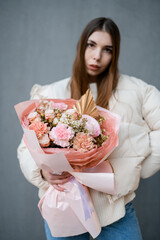 Girl with straight hair in puffy jacket on a gray background with a bouquet of pink peonies