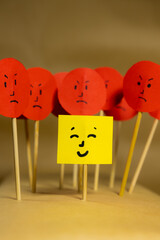 Vertical image of yellow paper with smiley face surrounded by angry faces, concept of social...