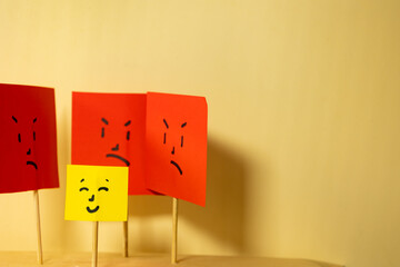 Horizontal image of yellow paper with smiling square face surrounded by angry square faces, concept...
