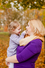 Plus-size woman in purple dress holding and playing with her 3-year-old daughter in autumn park