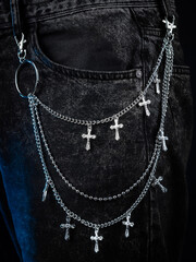Close up of silver metal chain with crosses in rocker style on jeans on grey background