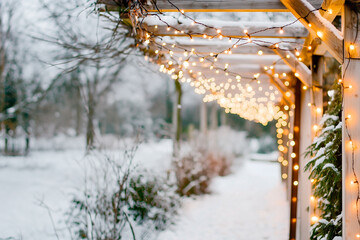String lights drape over a snowy garden trellis, creating a magical holiday atmosphere. The soft glow illuminates the winter scene, evoking a cozy, festive mood perfect for seasonal celebrations.