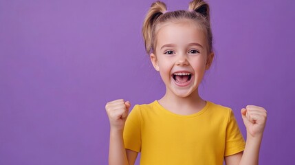 Naklejka premium A young girl with pigtails and a yellow t-shirt is smiling and making a fist with both hands. She is excited and happy.