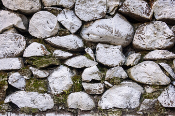 A close-up view of a stone wall composed of irregularly shaped, white stones with patches of moss...