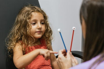Little girl taking pediatric eye exam with optometrist using red and blue sticks