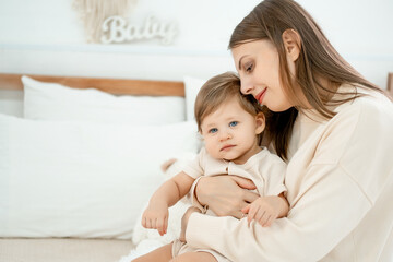 mom and baby on the bed at home hugging and kissing, mother and child playing and having fun, happy motherhood and a young family
