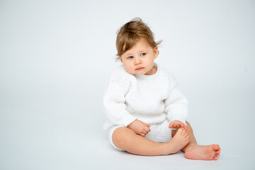A baby boy on a white isolated background with a place for text is sitting in white knitted clothes. A small happy child in a winter sweater , space for text