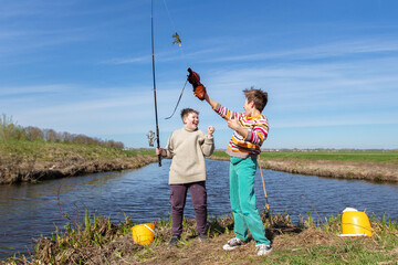 Funny fishing. Two of the boy's friends hooked an old shoe with a fishing rod and are laughing.