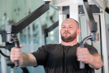 A man is working out with a machine that has a black handle. He is wearing a black shirt and has a beard