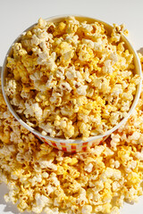 Close-up of gourmet popcorn in a clear container, spilling over onto the surface. Perfect for snack, movie night, or party themes, showcasing a crunchy and delicious treat.