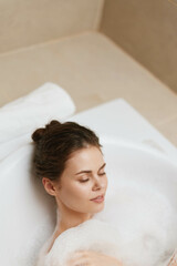 Relaxed woman enjoying a soothing bubble bath, surrounded by soft lighting and neutral tones. Self-care and wellness concept in a tranquil home setting.