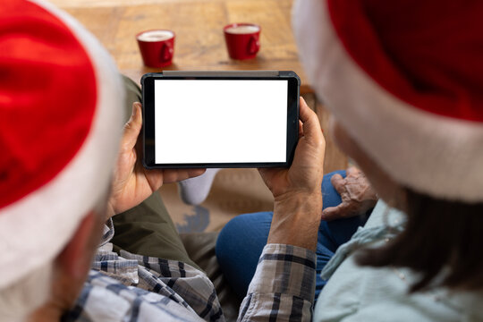 Senior couple wearing Santa hats using tablet at home during Christmas, copy space