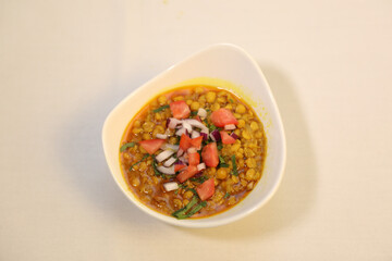 Deshi chotpoti garnished with fresh diced tomatoes, onions, and a sprinkle of green herbs.