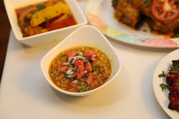 Deshi chotpoti garnished with chopped tomatoes and onions, surrounded by colorful sides including a vegetable curry and crispy fried items.