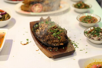 Juicy mutton curry garnished with fresh herbs, emitting flavorful steam with an array of small bowls filled with diverse sides, such as pickled vegetables and sauces.