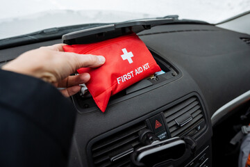 A person is holding a wellequipped first aid kit inside their car, which emphasizes the importance...