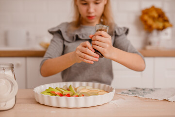 Girl in gray dress preparing apple pie, arranging apples on dough in Scandinavian style kitchen