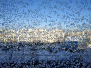 Snowflakes on window frost on glass city view background blue sky brightly lit houses yellow light...