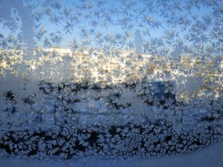 Snowflakes on window frost on glass city view background blue sky brightly lit houses yellow light New Year Christmas frosty natural pattern on winter window ice pattern with sunlight winter panorama