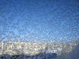 Snowflakes on window frost on glass city view background blue sky brightly lit houses yellow light New Year Christmas frosty natural pattern on winter window ice pattern with sunlight winter panorama