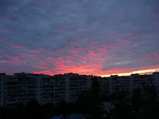 Bright unusual sunset city landscape orange pink rays above cityscape. Brutalist panel buildings appear as black silhouettes against a fiery orange-yellow sky dramatic lighting dark rain storm clouds
