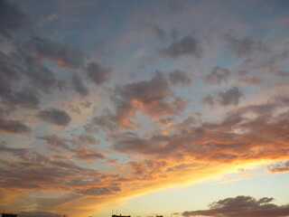 Bright unusual sunset city landscape orange pink rays above cityscape. Brutalist panel buildings appear as black silhouettes against a fiery orange-yellow sky dramatic lighting dark rain storm clouds