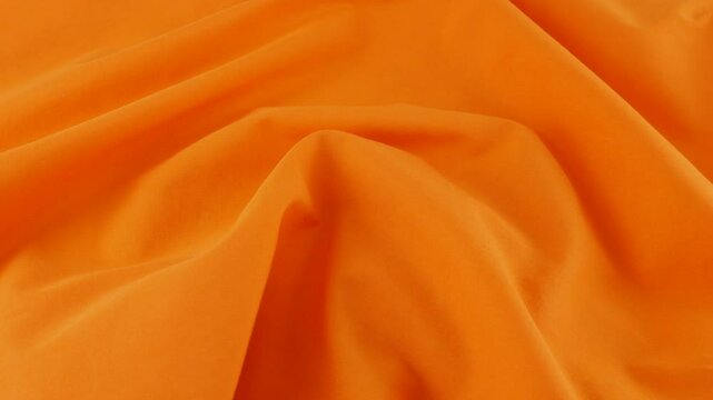 Top view of the soft folds of the  royal orange cotton fabric. The textile background rotates on the display case. Background on the theme of fashion, design, natural fabrics, shades of color.