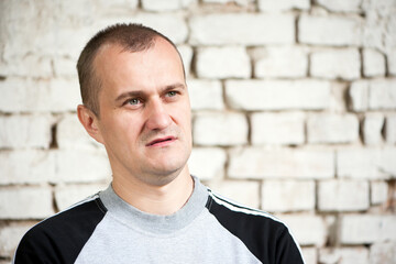 Young European. man portrait. the guy is standing against a brick wall. photo, smiling, thoughtful, surprised, indignant, feelings, emotions. fair skin, slight stubble. man 30-40 years old. close-up